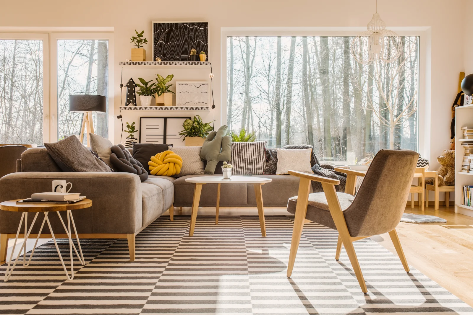 Sunlit Scandinavian living room with a gray sofa, tall windows, and winter trees beyond